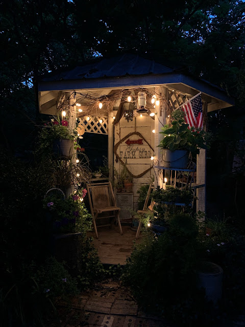 Rustic gazebo at night time with upcycle garden containers and flowers