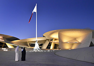 Arabian couple at museum with Qatar flag flying in blue sky