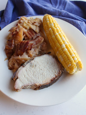 Juicy pork loin wrapped in bacon and cooked on the grill is loaded with flavor. It is a great way to feed your family or a crowd. Make a whole loin or part of one and enjoy a fabulous dinner! dinner plate of bacon wrapped pork loin, corn on the cob and bacon wrapped beer braised cabbage