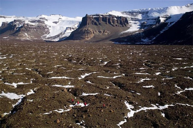Для масштаба долину пересекает команда геологов (красненькие). Их влечет ледник на заднем плане, что содержит в своих слоях историю климата многих веков.