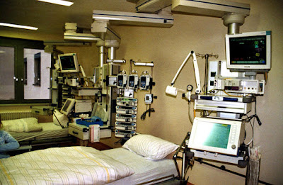 A hospital intensive care bed, with pumps and a ventilator next to it