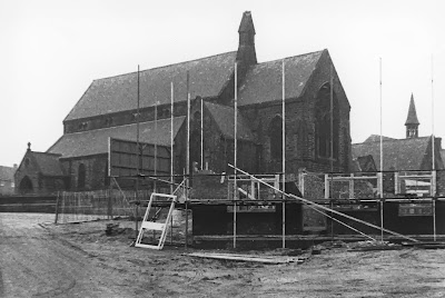 Grayscale photo of a church in the background and a half built structure with scaffolding surrounding it in the foreground.