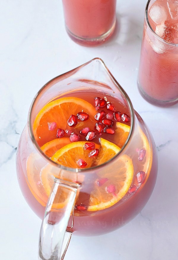 a close look at the picher with Christmas morning punch with pomegranate arils orange slices on a white backdrop