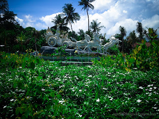 Fertile Garden Plants With Krishna's Chariot Statue Of The Park At Tangguwisia Village, North Bali, Indonesia