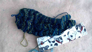 A partially finished textured knit glove.  Two fingers are finished, and a third finger is tucked inside a fabric double-pointed needle case.  The ends have not been woven in.