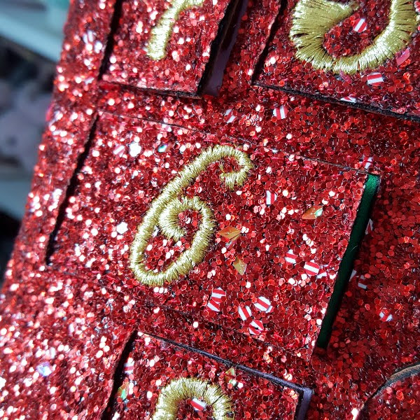 close up of red glitter advent boots with candy striped pieces and embroidered numbers on doors