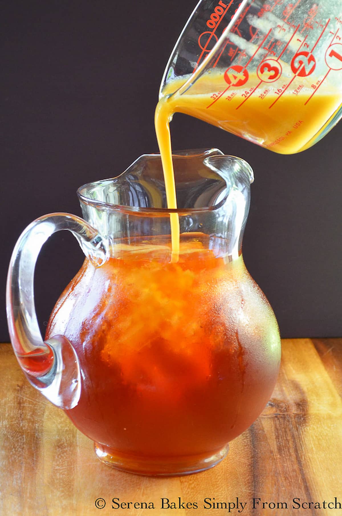 Peach Puree being poured into ice tea in a large glass pitcher.
