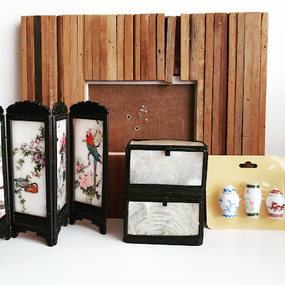 Rustic picture frame with various wood lengths on it behind a dolls' house Asioan screen, two small boxes made with black metal and clear shell, and a mint in package set of three 1/12 scale miniature ginger jars.