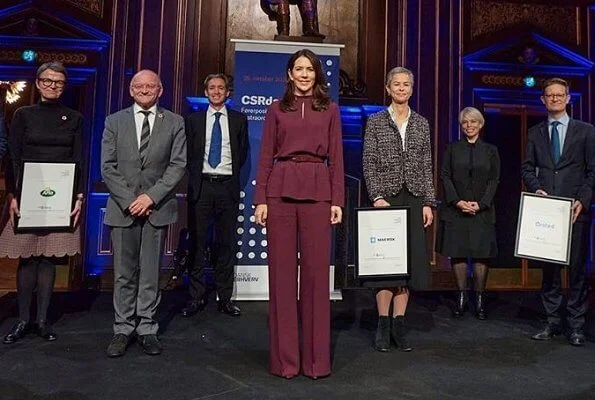 At the award ceremony, Crown Princess Mary wore a burgundy silk mock neck belted top and trousers, and grey cashmere wool long coat