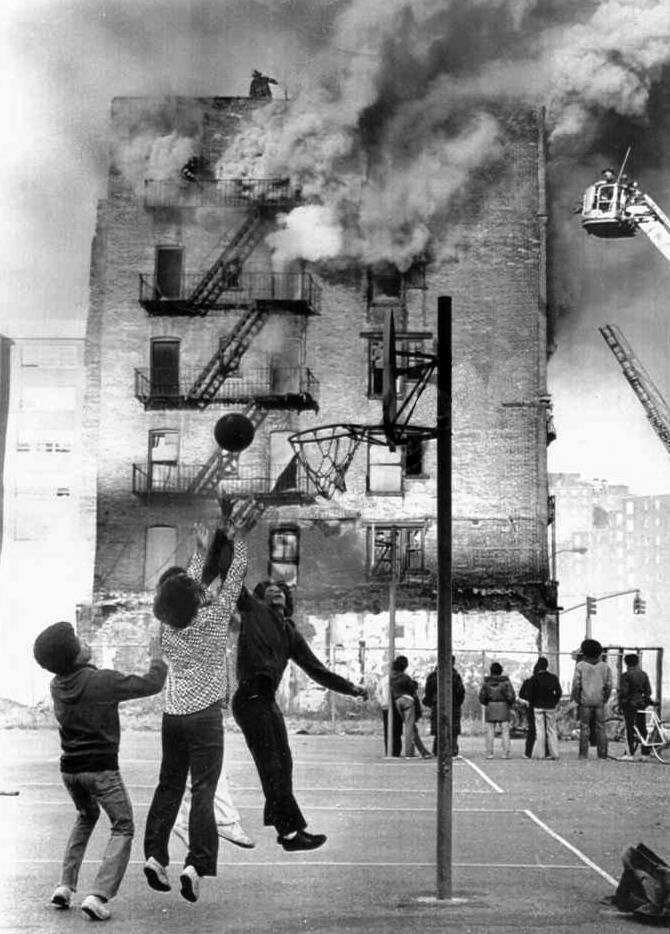 Young boys ignore a 1975 apartment building fire while playing basketball in front of the blaze. Baskets and Ladders. marchmatron.com Young boys ignore a 1975 apartment building fire while playing basketball in front of the blaze. Baskets and Ladders. marchmatron.com
