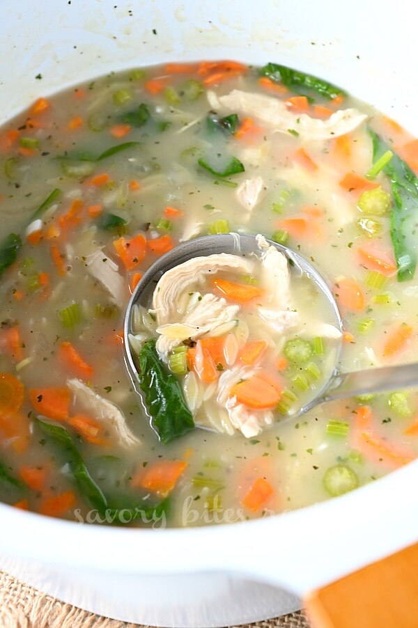 a spoon scooping chicken orzo soup in a white pot