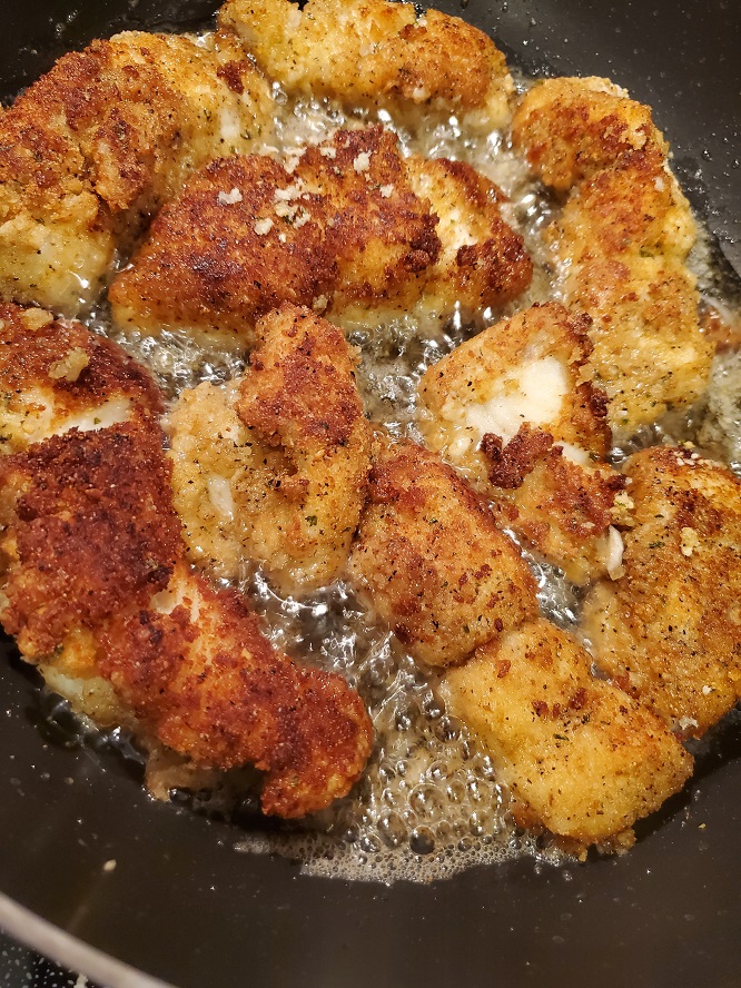 this is a huge fry pan with fish frying in it coated with panko bread crumbs