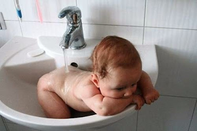 Lustiges Baby fühlt sich wohl im Waschbecken - Abkühlung im Sommer Lustiges Baby fühlt sich wohl im Waschbecken - Abkühlung im Sommer