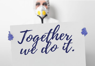 A masked nurse wearing gloves is holding a sign that says together we do it.