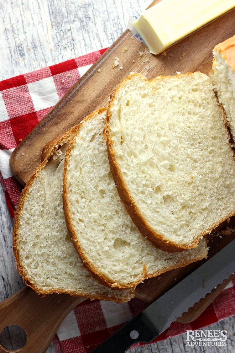 Three slices, overhead view, of soft white bread with on a wooden board with butter on the side