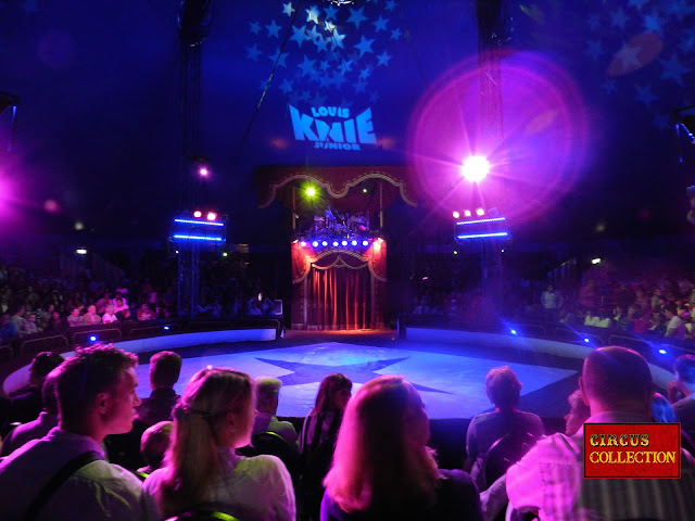 L'intérieur du chapiteau du cirque Louis Knie junior  avec le rideau de velours rouge et l'orchestre