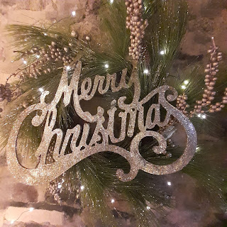 Sparkly gold lettering in middle of a pine wreath, reads 'Merry Christmas.'