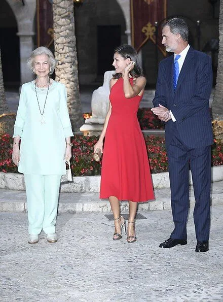 scoop neckline sleeveless fit and flare red dress. Dolce & Gabbana ready-to-wear collection, gold clutch. Queen Sofia