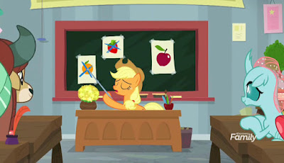 In front of a class containing Yona and Ocellus, Applejack sits at a teacher's desk, pointing to drawings of fruits on a blackboard. All but the apple are crossed out.