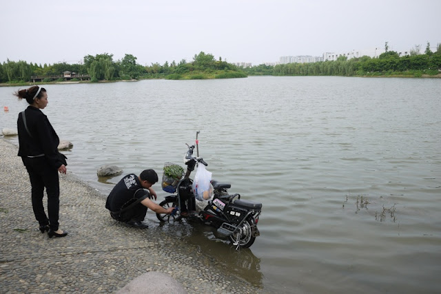 man washing motorbike while woman watches