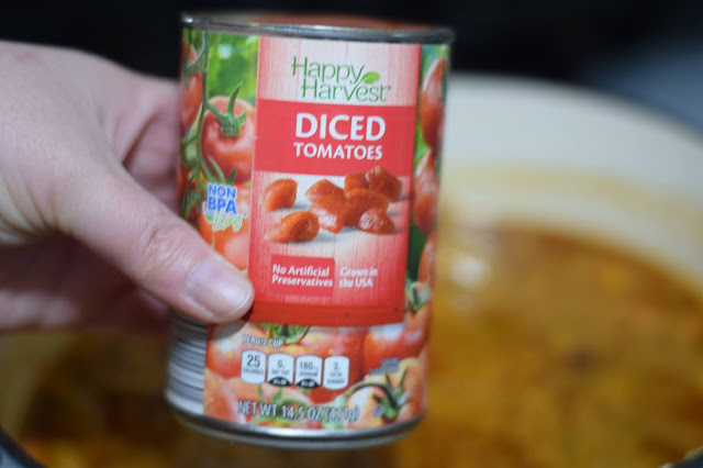 The can of diced tomatoes being added to the dutch oven.