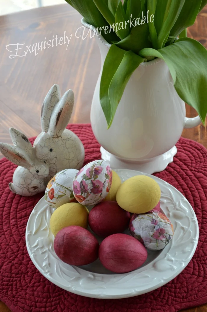 Decoupage Easter Eggs With Napkins, bunny figures and flowers in a pitcher on a table