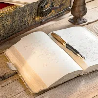 年季の入った古い木の机の上に小さな使い古されたノートがびっしり文字の書かれた開いて置いてあり、その上に万年筆が置いてある写真.jpg (1600×1600)