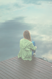A young lady sitting alone on a dock.