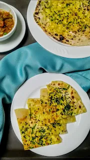 Small pieces of paneer kulcha in a serving plate, mix veg and kulcha in background