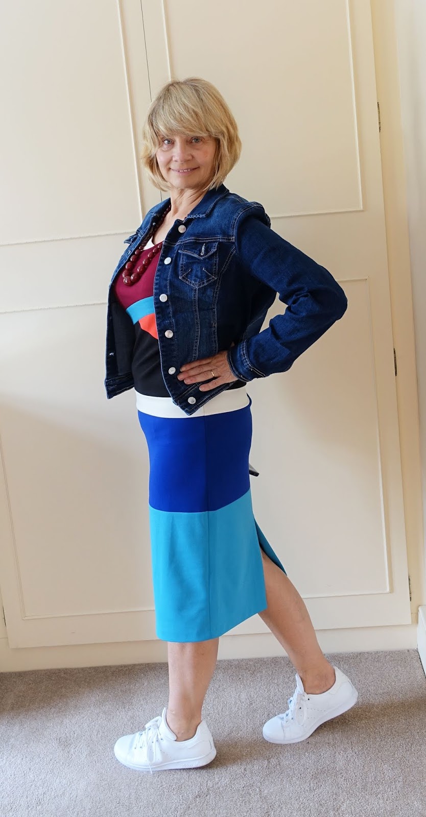 Fair haired woman in colour block dress denim jacket and white trainers