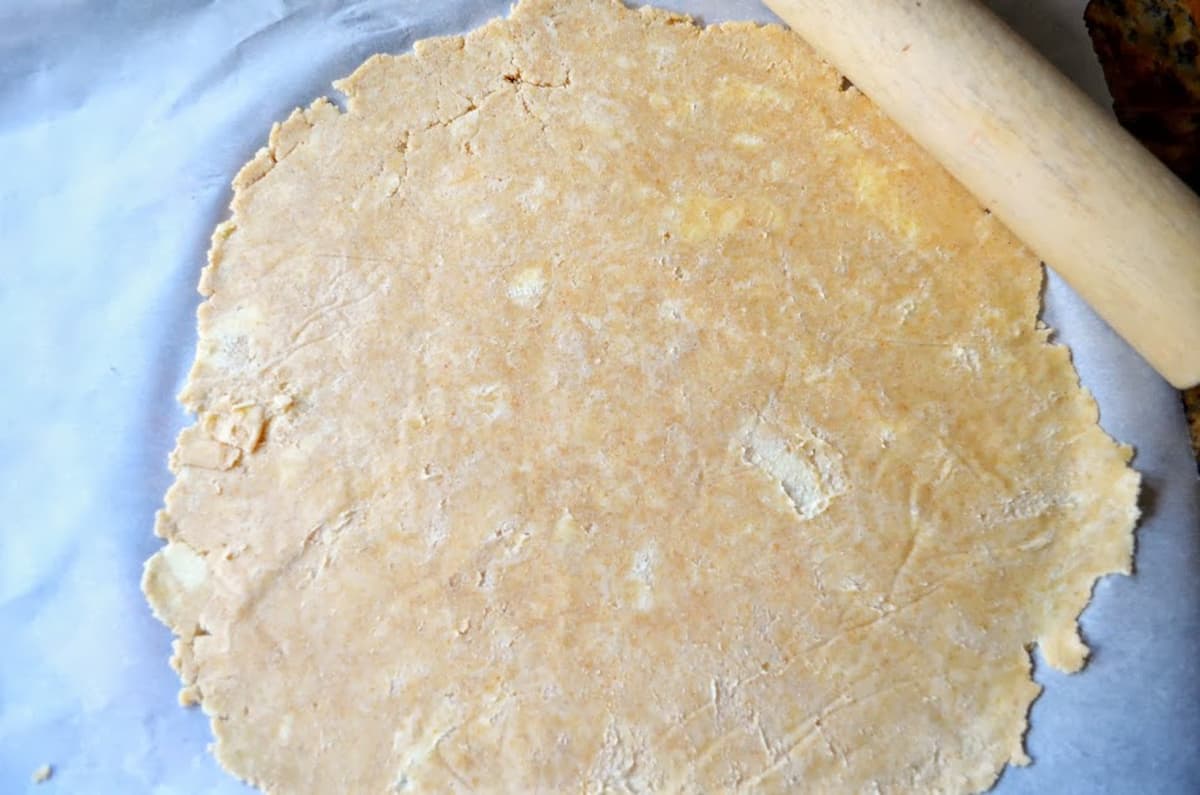 Flaky Sour Cream Pie Crust rolled out on a piece of parchment paper with a rolling pin on the corner of the dough.