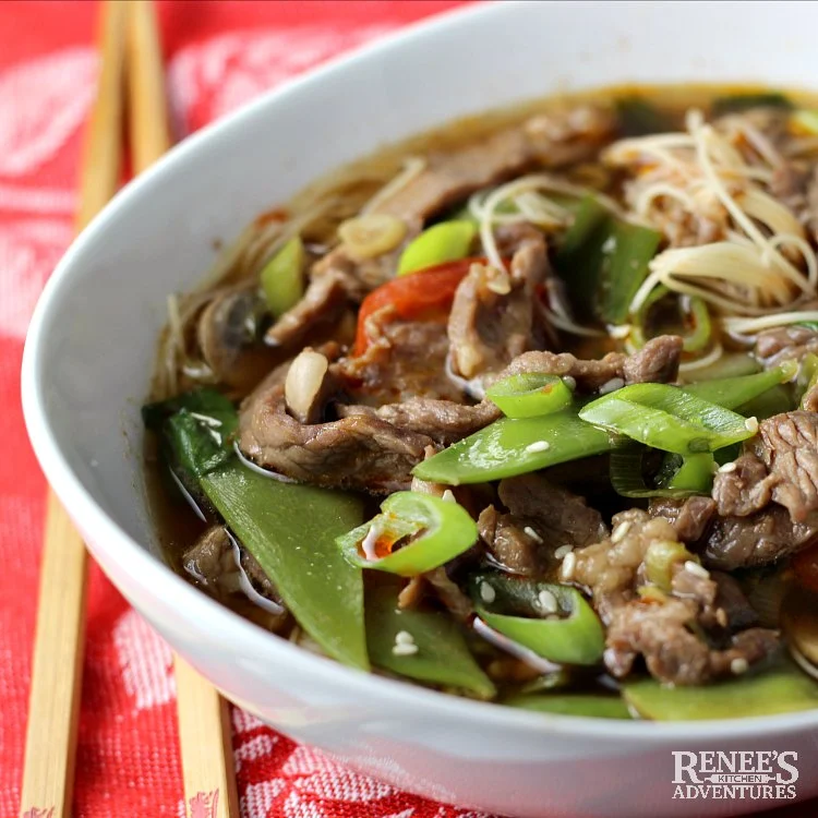 Spicy Chinese Beef Noodle Soup by Renee's Kitchen Adventures in a white bowl with a set of chopsticks next to the bowl on a red napkin