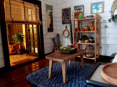 One twelfth scale modern miniature holiday house lounge with white shiplap walls and french doors opening out onto a courtyard.