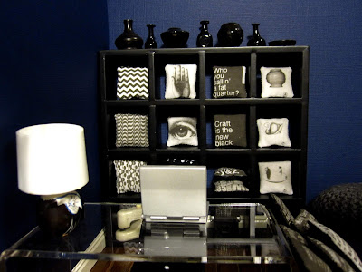 1/12 scale cushion shop with a laptop on the sales table and a cube bookcase of black and white cushions behind.