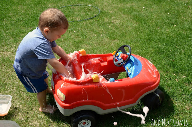 Toddler washing a ride on car with colored soap foam