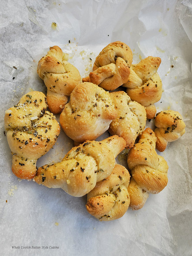 Italian style dough made into garlic knots rolled into oil and herbs with spices on wax paper