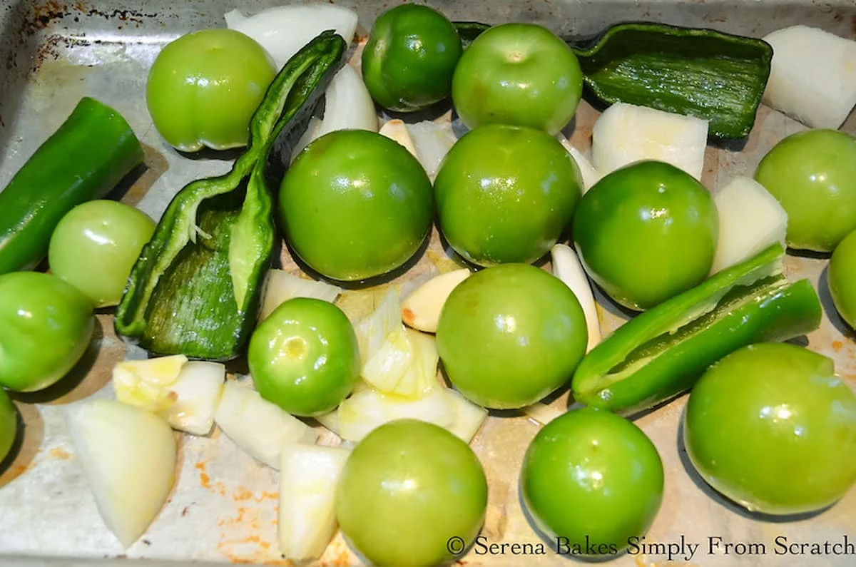 Peeled Tomatillos, Poblano Peppers, Jalapeños, Garlic, and Onion drizzled with oil and salt on a metal baking sheet.