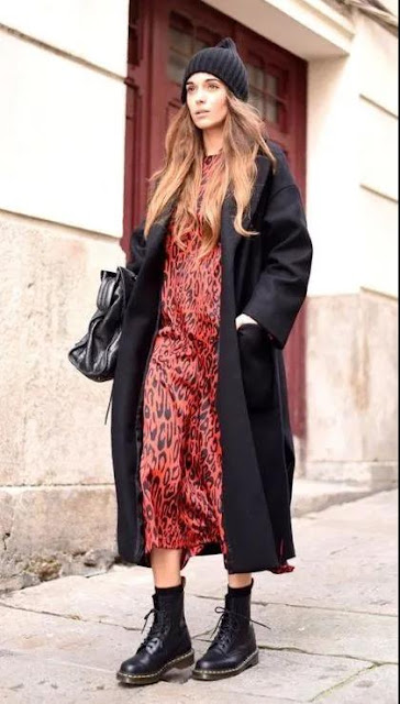 A woman wear a black coat and a printed skirt.