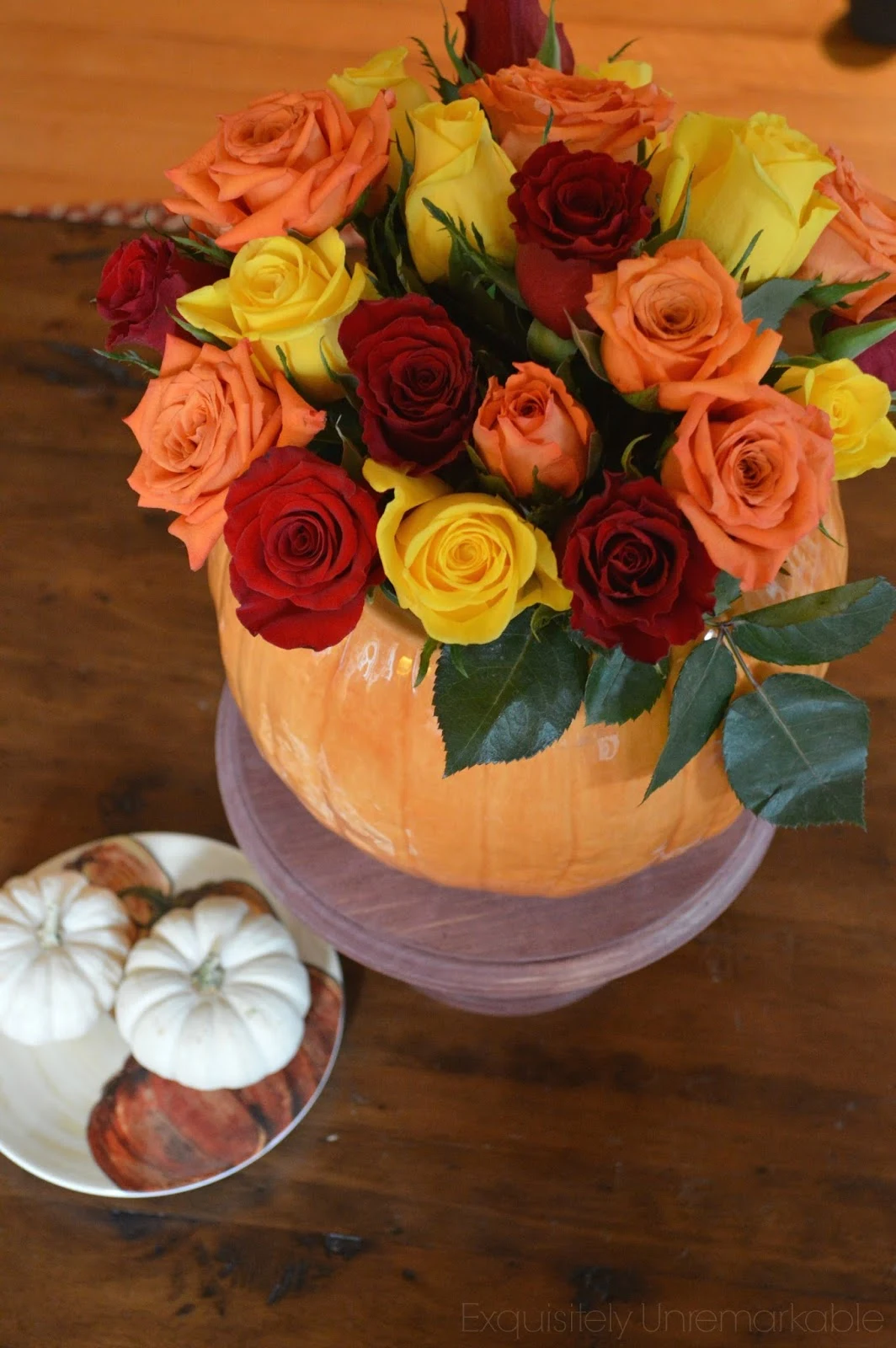 Pumpkin vase rose Floral Arrangement on cake stand with small pumpkins on a pumpkin dish nearby