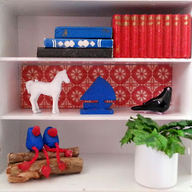 One-twelfth scale miniature retro display shelving containing books, a pot plant, glass bird and various other objects.