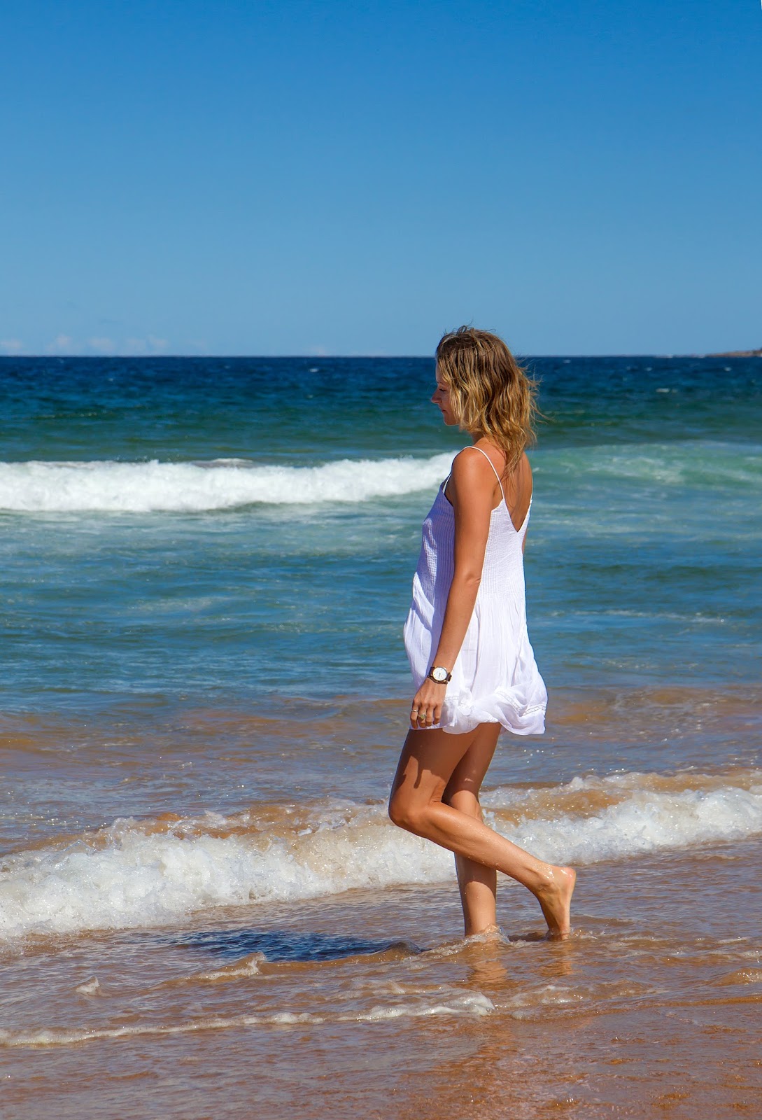 fashion and travel blogger, alison hutchinson from Styling My Life is playing in the waves at Palm Beach in Sydney, Aystralia in a white Zara sundress.