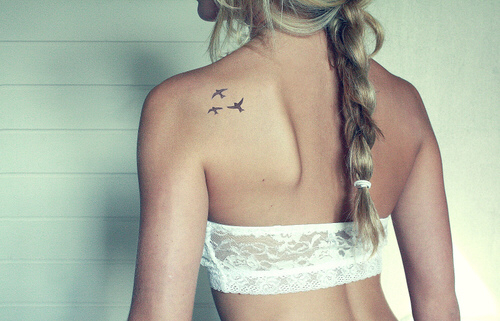 Chica mostrando su tatuaje en forma de tres aves que tiene sobre la espalda