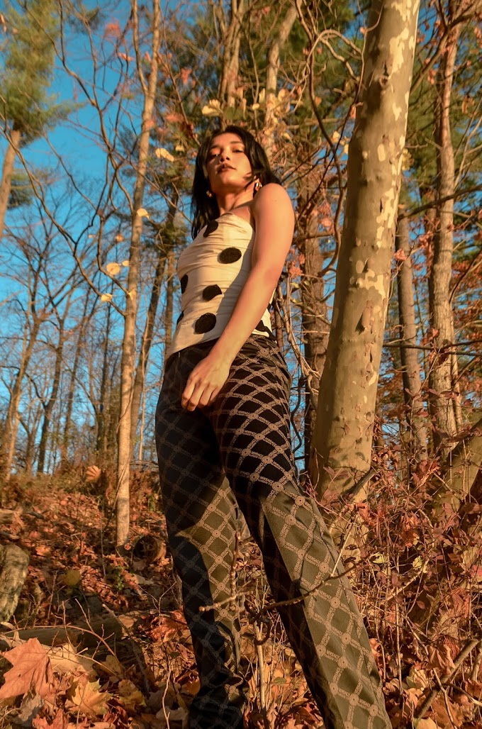 View from lower level Versace logo pants, brown beige medusa logo, Jacquemus polka dot top strapple top, beige top with black dots, trees and leaves and a lake in the background, fall mood, North Salem, NY 2020