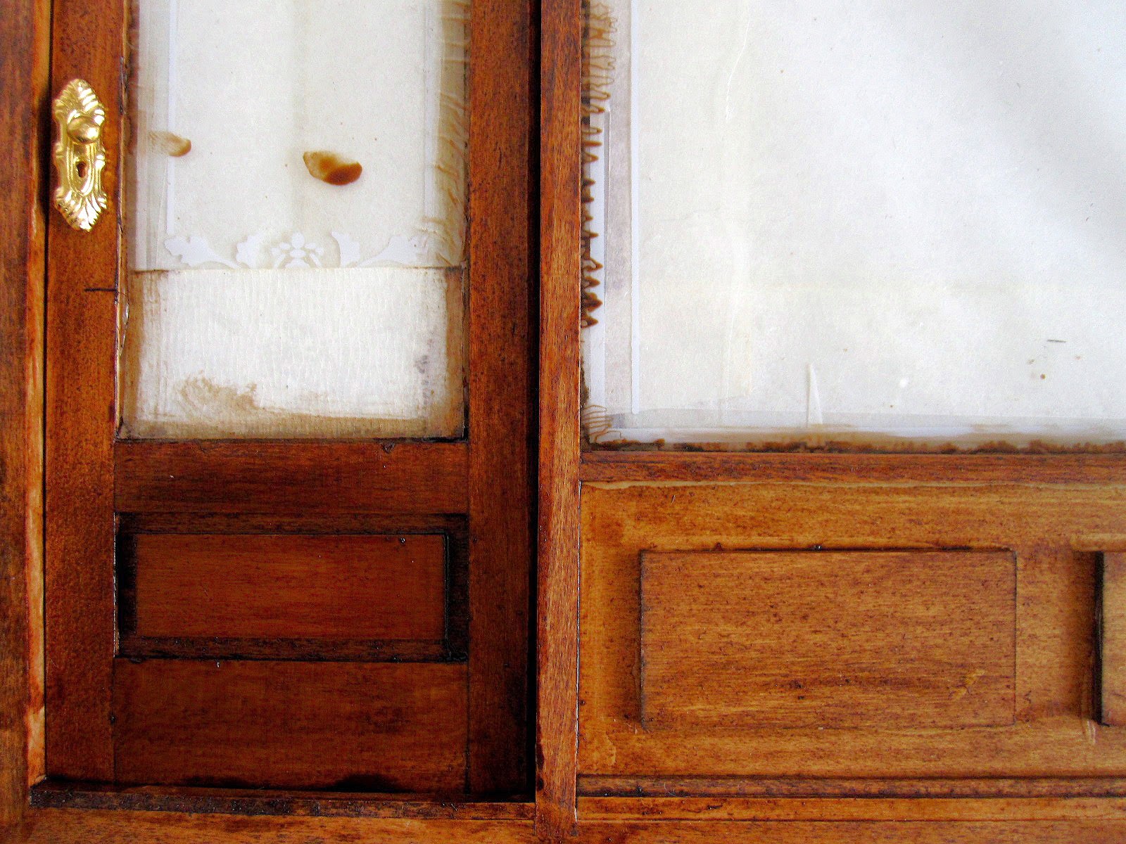 Modern dolls' house miniature shopfront under renovation, showing papered-up windows and varnished door and walls.