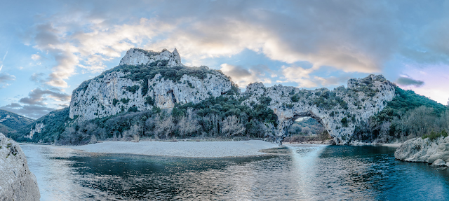 Veduta panoramica del Pont d'Arc, un arco in pietra sul fiume con le montagne della Grotta Chauvet sullo sfondo. © David Huguet