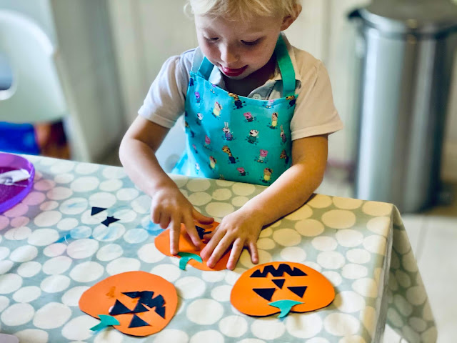 Preschooler with her tongue out sticking the face on to 2D cardboard pumpkins