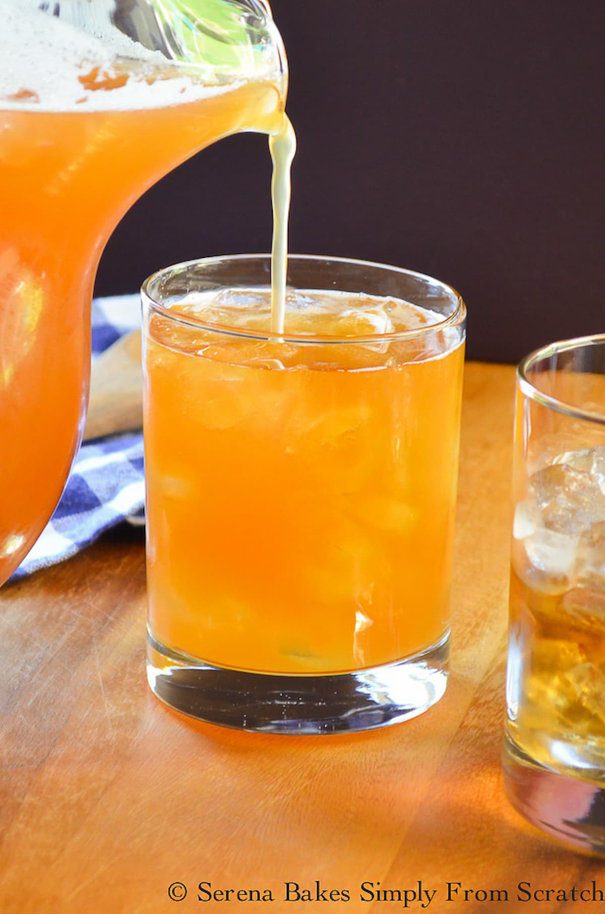 Peach Whiskey Iced Tea being poured from a pitcher into a glass filled with ice.