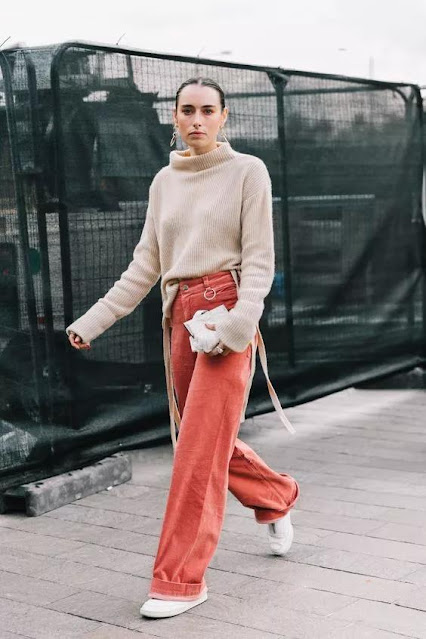 The woman wears a sweater and wide-leg pants.