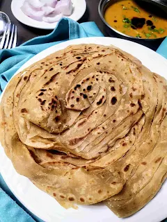 Serving wheat parotta in a plate, dal and onion slices in background