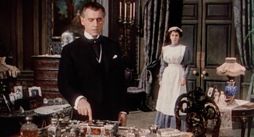 A man looks at his desk while a maid stands in the background.